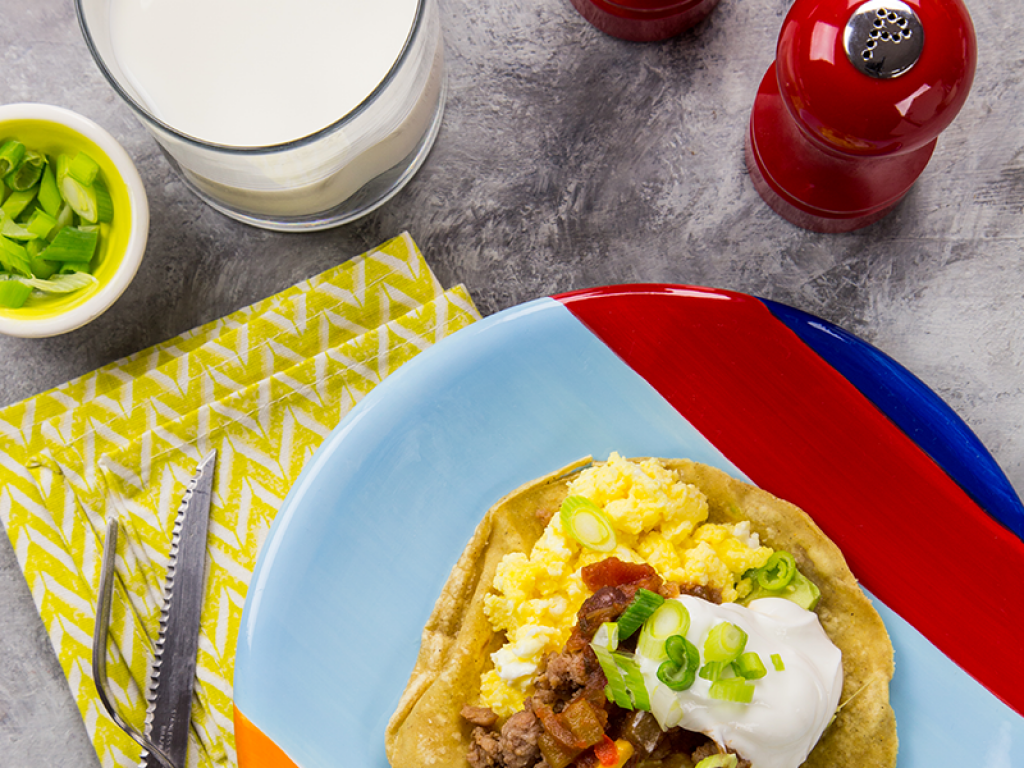 Aerial shot of huevos rancheros on a colorful plate next to a glass of milk.