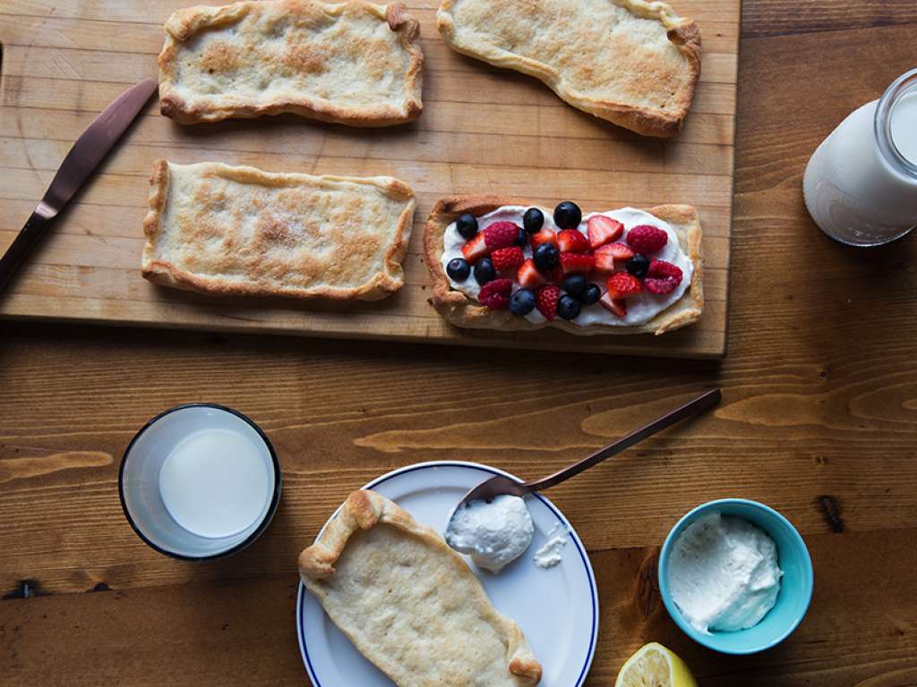 Aerial shot of a cutting board with dough on it with yogurt and berries on top of one piece.