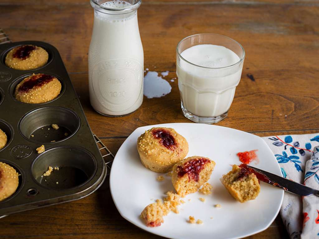 Aerial shot of muffins with jam on top on a white plate with a glass of milk next to it.