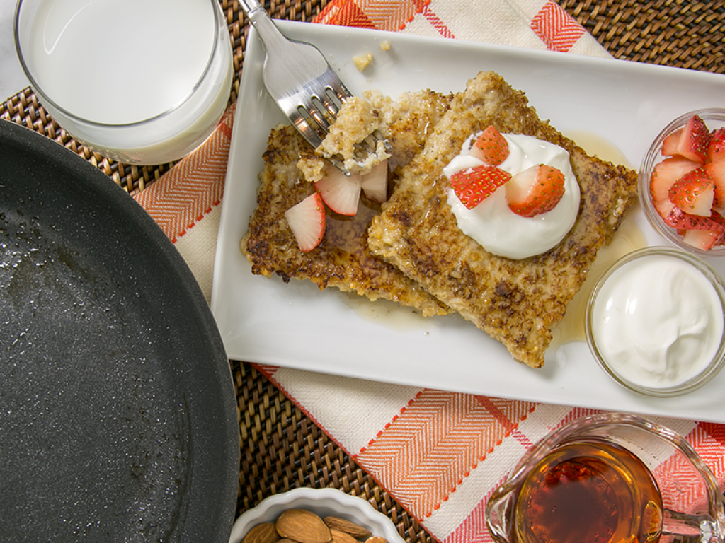 Aerial shot of pancakes with whipped cream and strawberries on top with a glass of milk next to it.