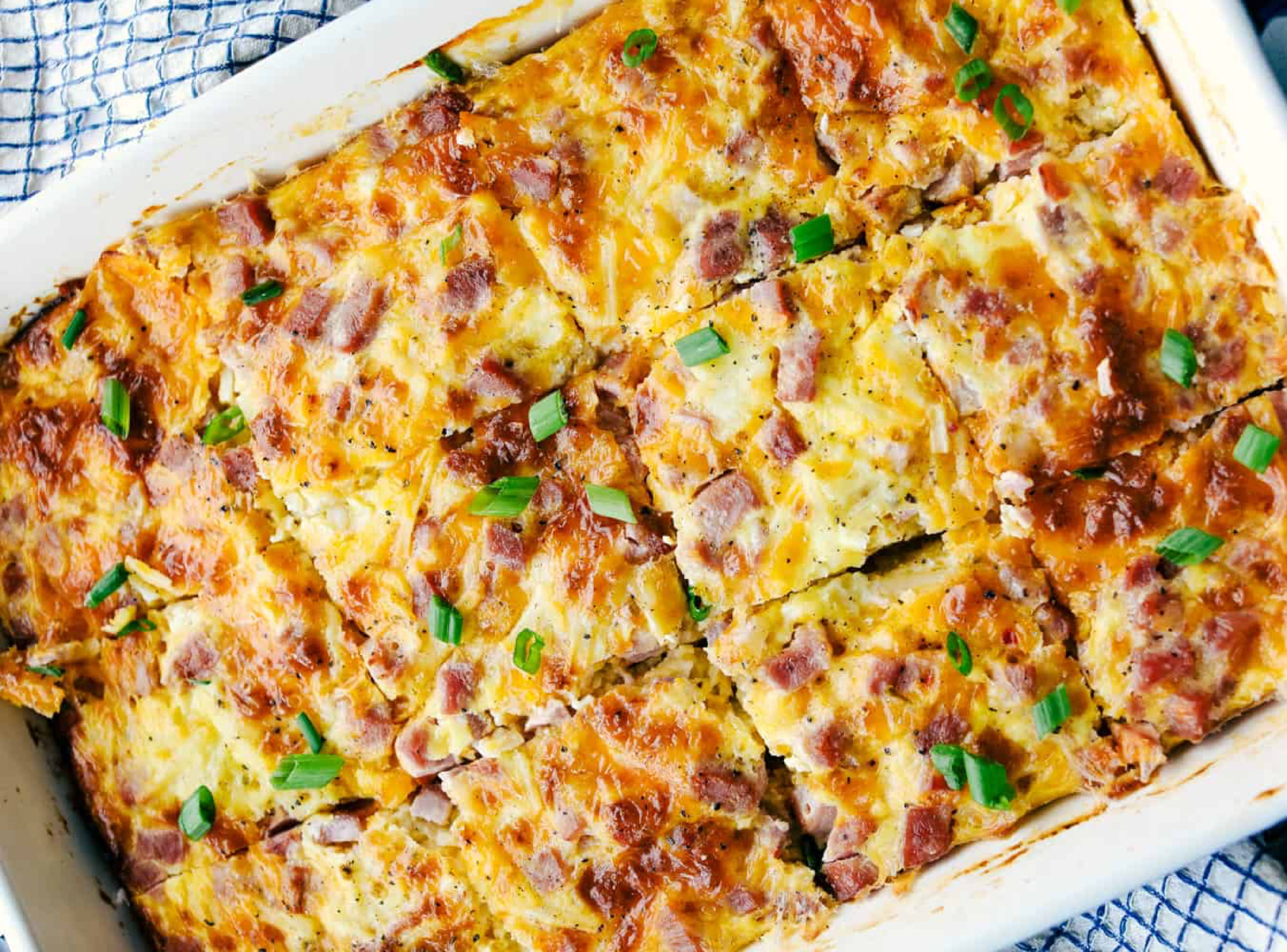 Egg and pepper casserole in a white dish. Cut into twelve squares and green onions on top for garnish.