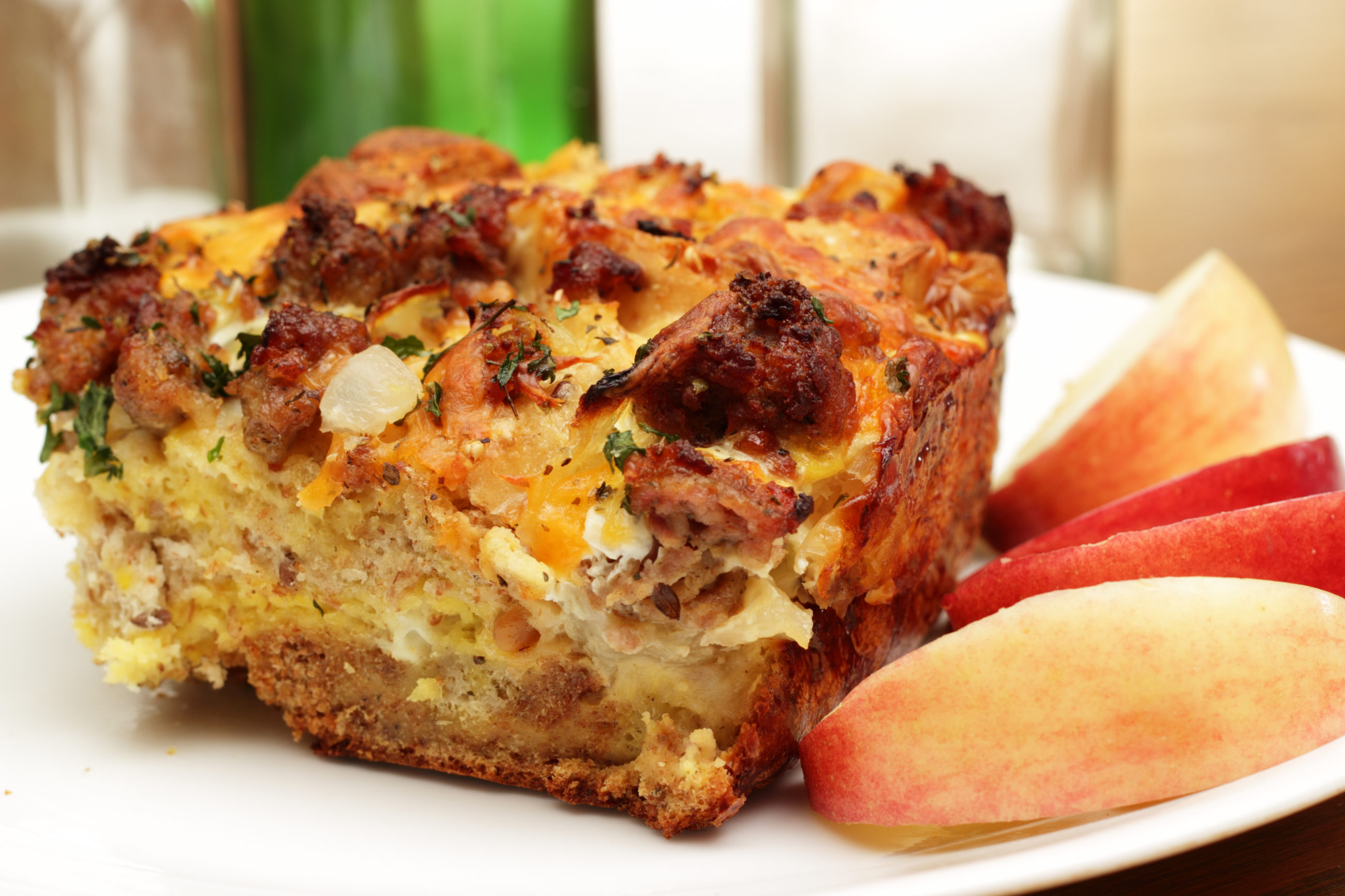Piece of bread pudding on a white plate with a side of sliced apples.