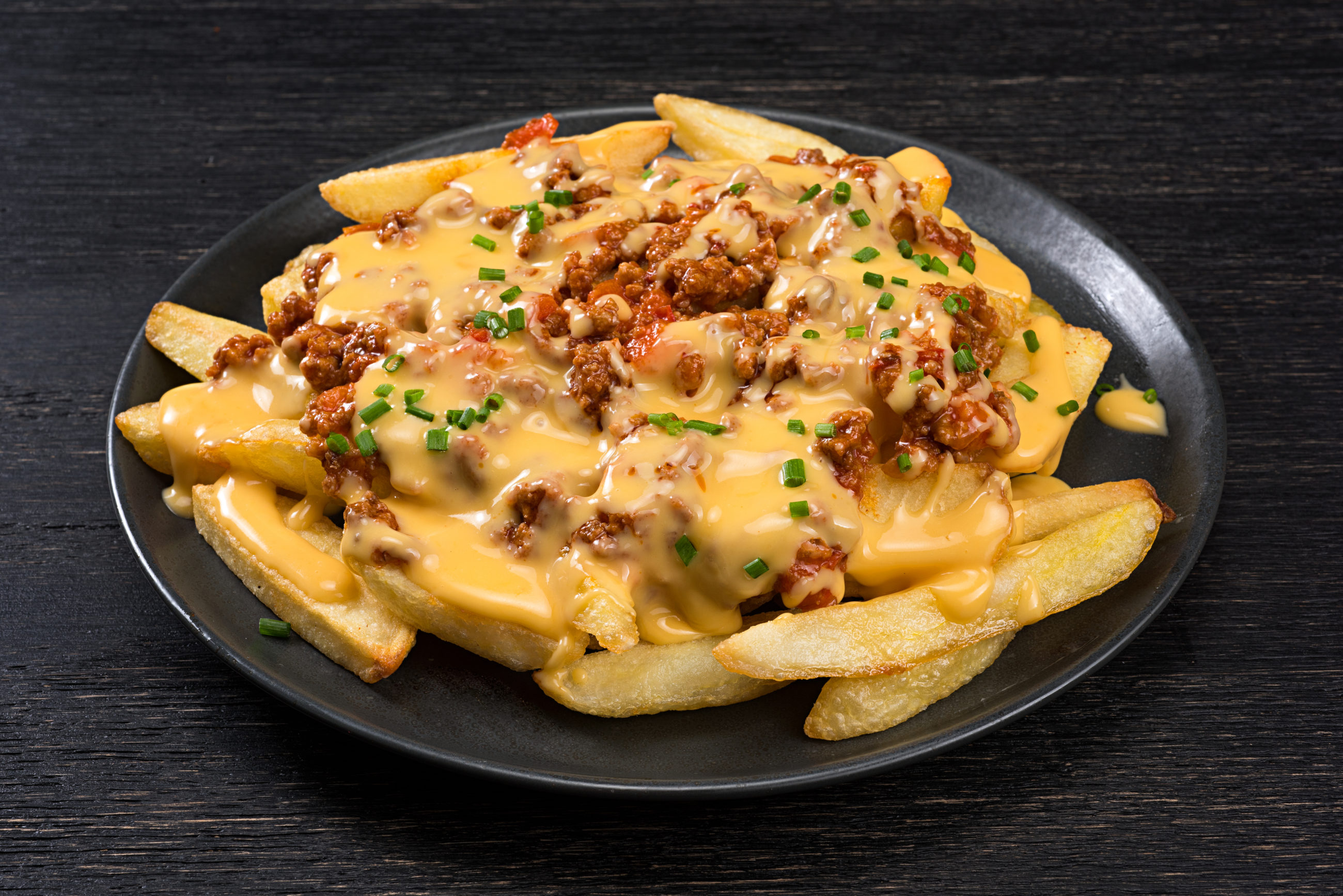 Bacon and cheddar cheese fries on a black plate