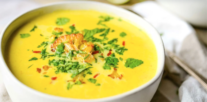 Curry Cauliflower Soup in a white bowl with roasted cauliflower, cilantro, and sriracha as garnish.