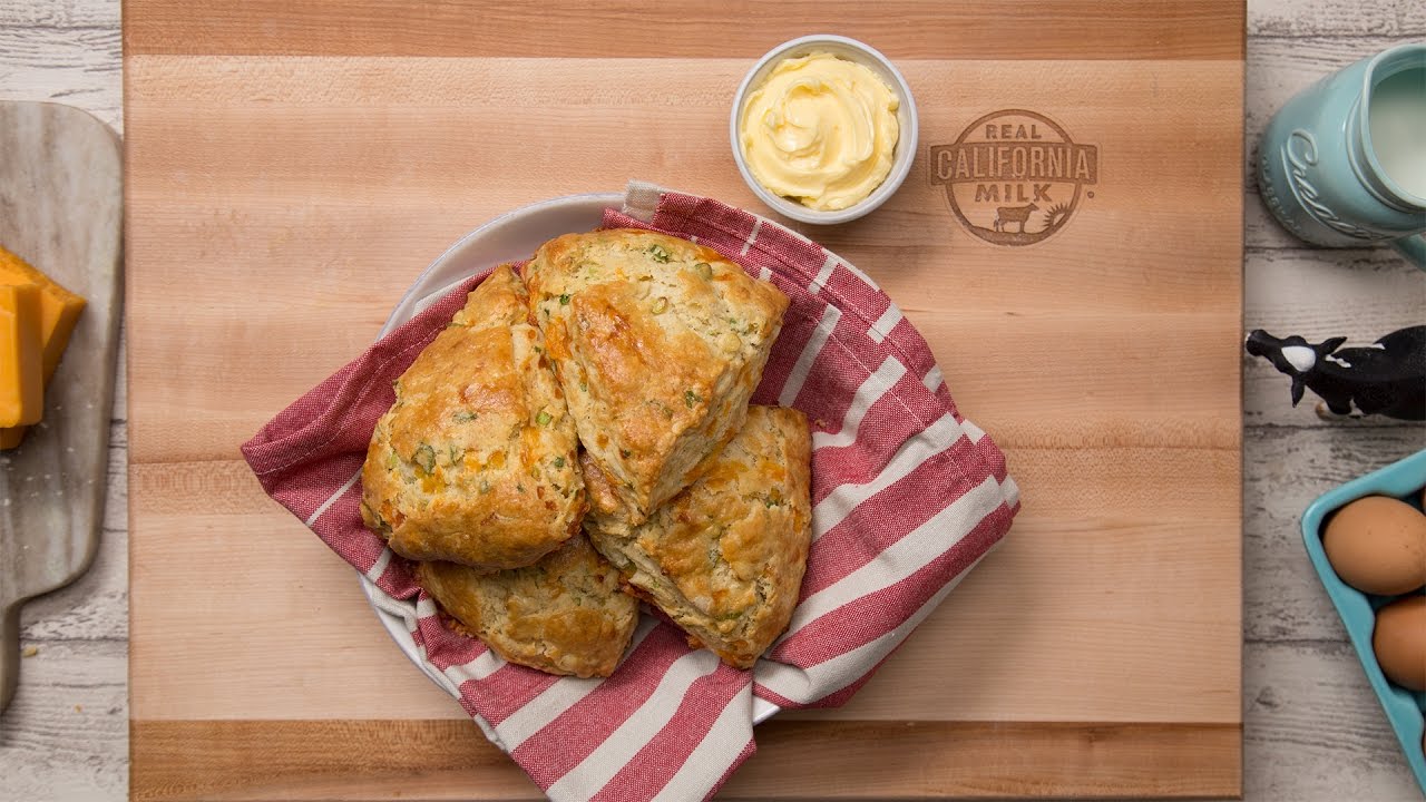 Cheddar and Green Onion scones in a white bowl with a red and white stripe kitchen towel. A small bowl of butter on the side and on top of a cutting board.