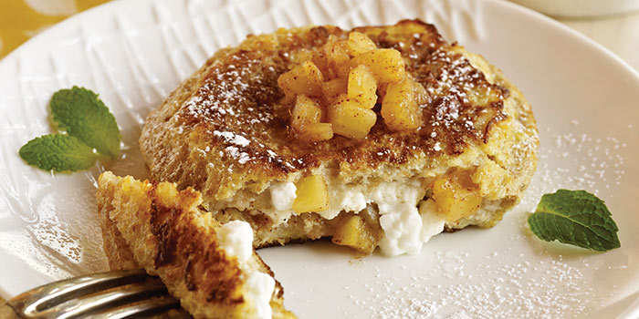 Pineapple stuffed french toast with a piece cut off on a fork on a white plate. Pineapple, powdered sugar, and mint to garnish.