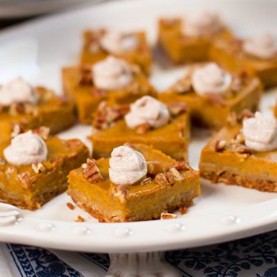 Pumpkin Pie squares with chopped pecans and a dollop of cinnamon sugar yogurt topping on a white serving platter.
