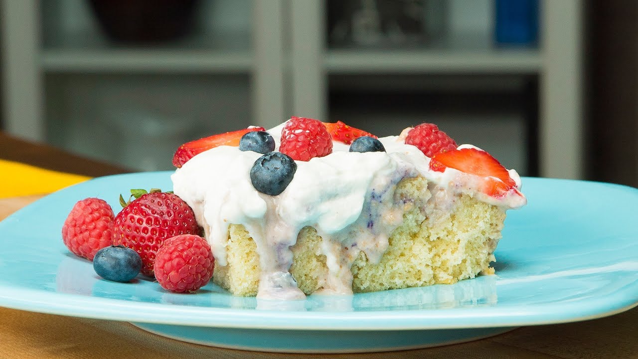 Tres Leches Cake with Vanilla Frosting and strawberries, raspberries, and blueberries on top. On a blue plate.