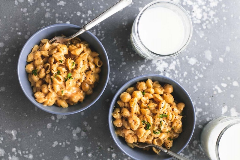 two bowls of creamy mac n cheese and a glass of milk on a grey counter top