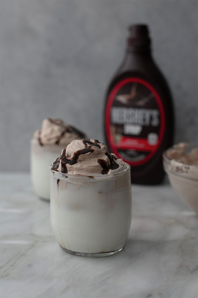 small glass with milk shake and bottle of Hershey's syrup in the background