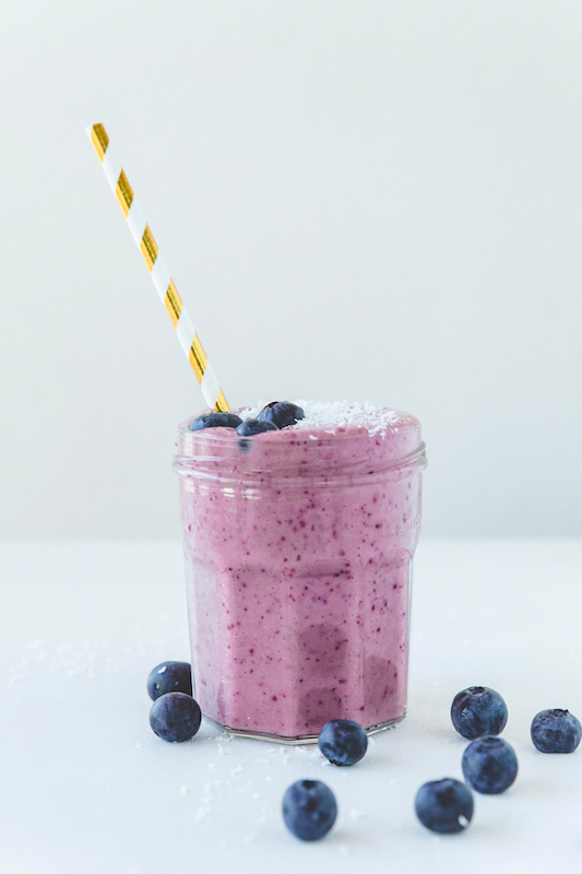 glass with purple smoothie and striped straw along with blueberries.
