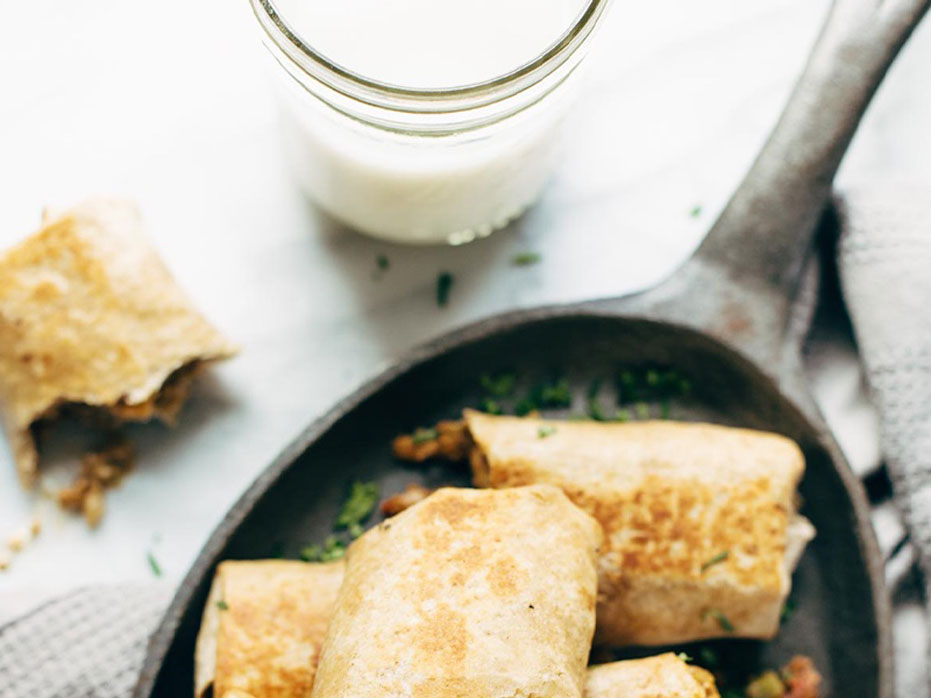 Aerial shot of breakfast burrito cut in half with a glass of milk on the side.