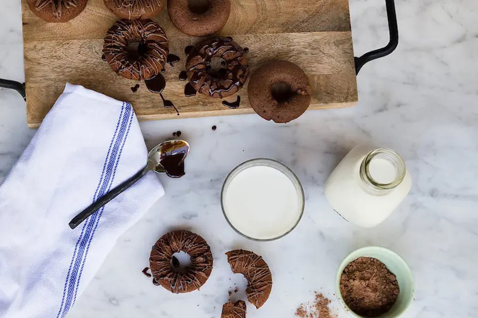 aerial shot of chocolate donuts with a glass of milk on the side.