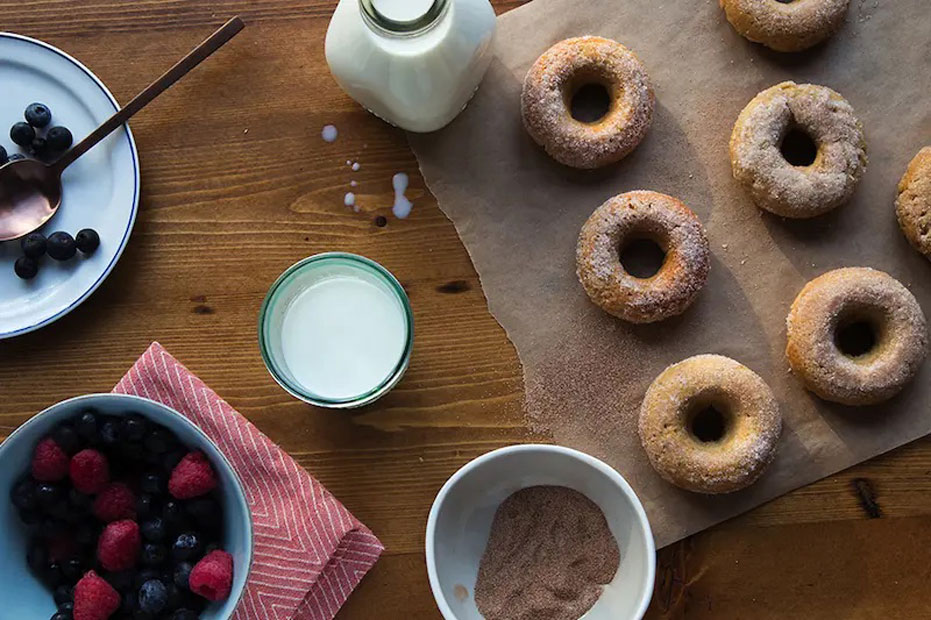 aerial shot of 5 donuts on parchment paper, with a glass of milk and two bowls of mixed berries on the side.