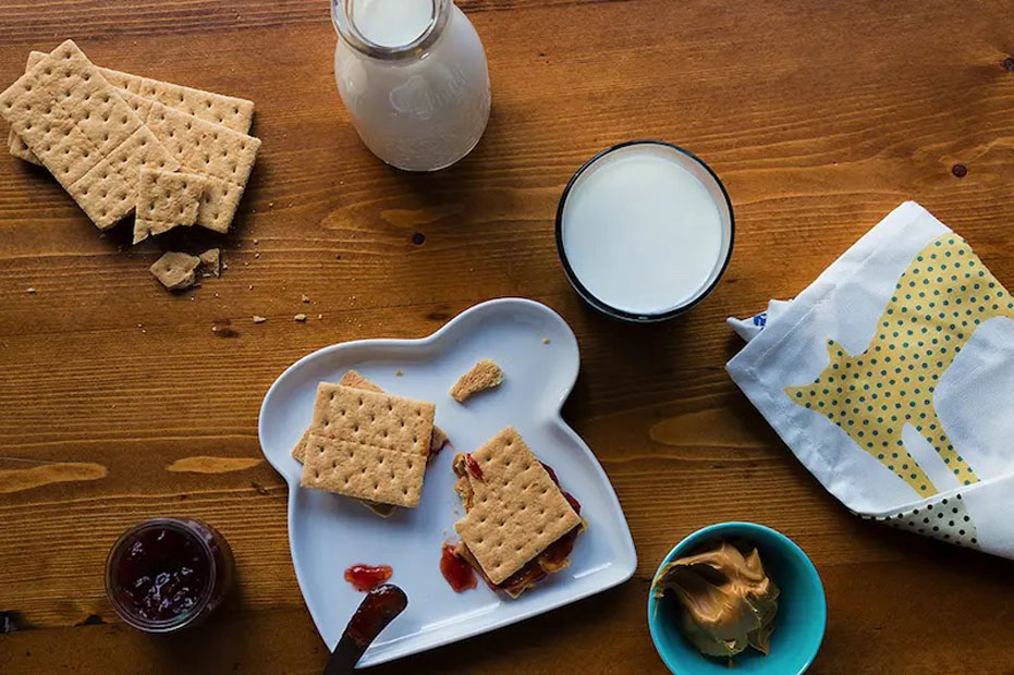 Aerial shot of graham cracker pb&j on a plate. graham crackers, glass of milk, and side bowls of jelly and peanut butter on the side