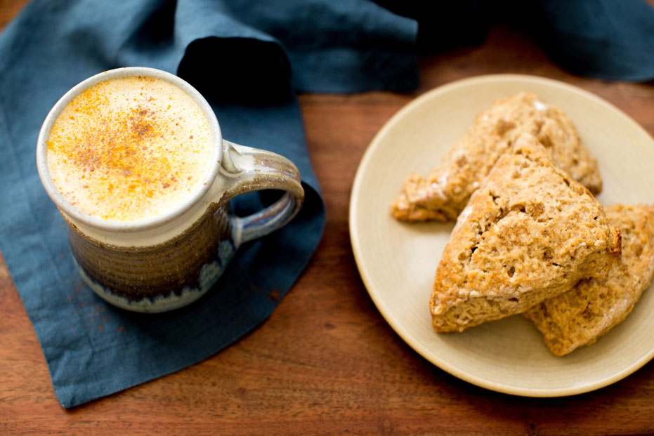 aerial shot of pumpkin latte in a glass mug with a plate of three scones on the side.