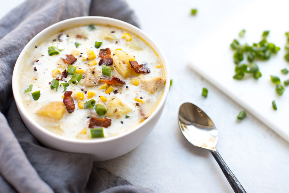 aerial shot of corn chowder with bacon and scallion garnish. silver spoon with scallions on the side in the background