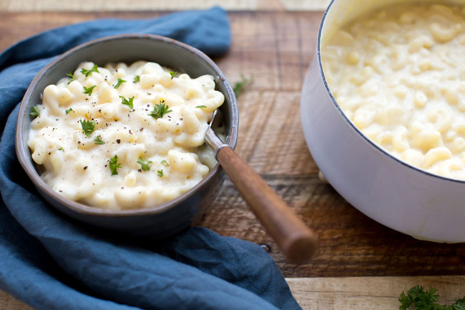 bowl of cauliflower mac n cheese, next to a pan of entire dish. blue napkin on the side