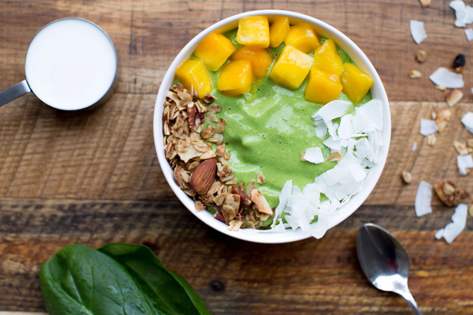 bowl of green smoothie with fruit, nuts and coconut