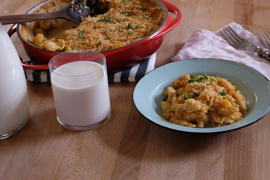 bowl of mac and cheese with a glass of milk and large dish in the background