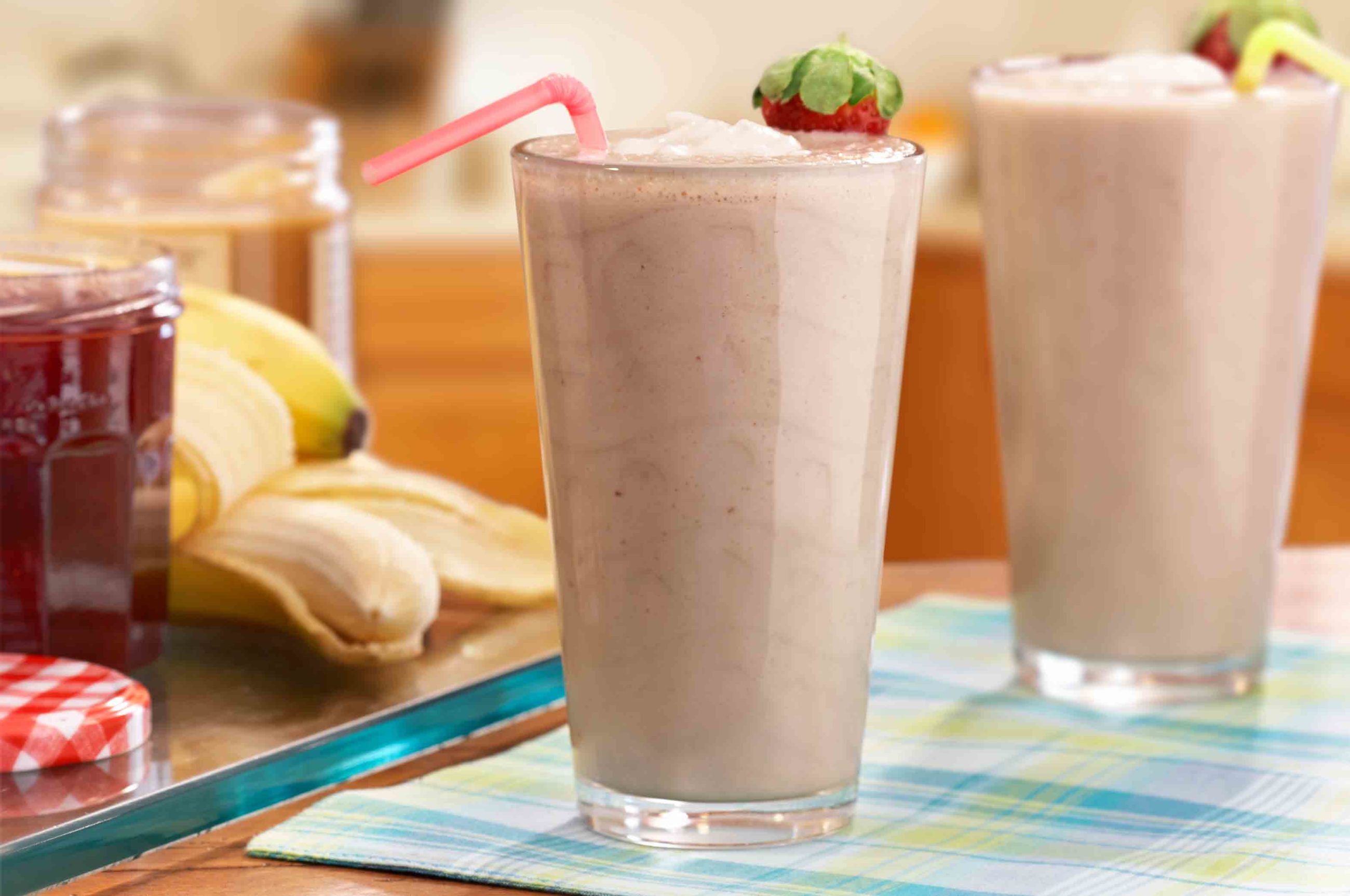 purple smoothie with strawberry garnish next to fruit preserves and peanut butter on checkered placemat