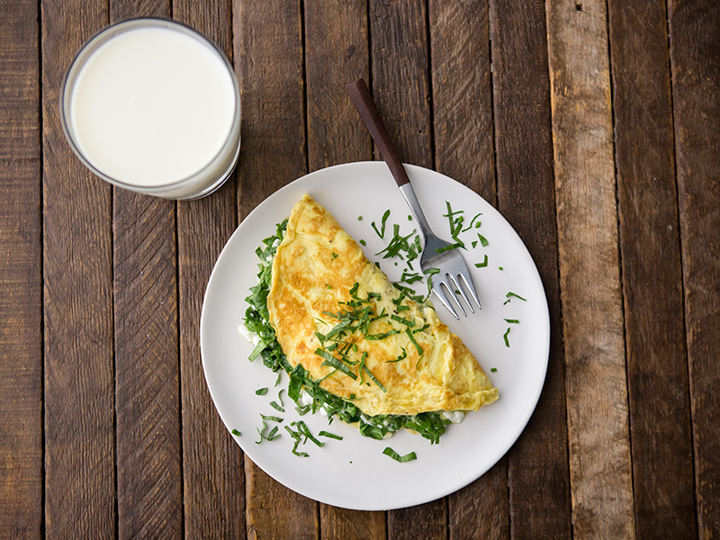 aerial shot of an omlet with chives and herbs, on a wood table, with glass of milk